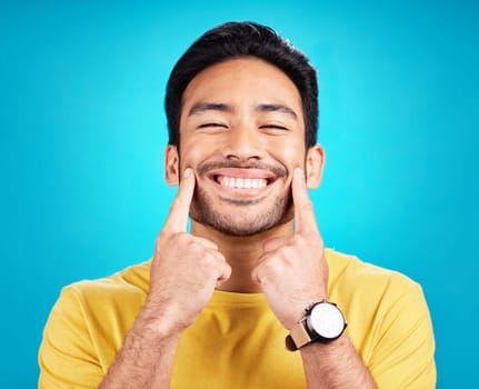 Teeth, smile and pointing with a man on a blue background in studio for dental care or oral hygiene. Portrait, face and happy with a handsome young male at the dentist for tooth care or whitening.