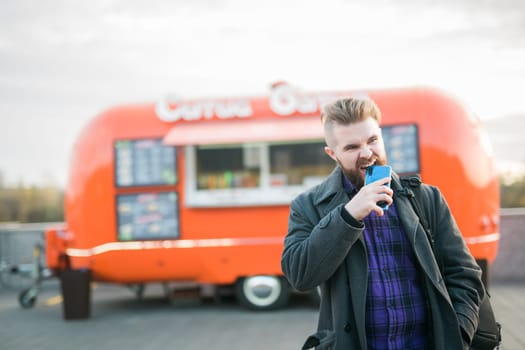 Angry hungry man bites smartphone on background food truck - hunger and lack of money
