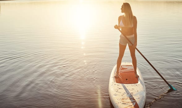This is where she comes to think. an attractive young woman paddle boarding on a lake.