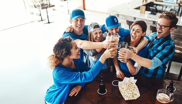 Sports fans make up a sports family. a group of friends toasting with beers while watching a sports game at a bar.