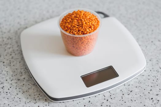 Lentils in a plastic measuring cup on an electronic kitchen scale