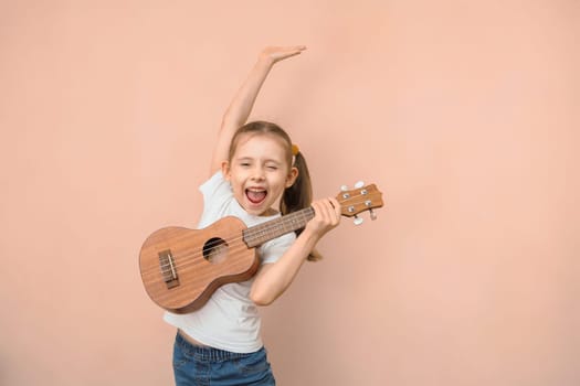 Expressive emotional Caucasian girl of primary school age learns music by playing the children's guitar