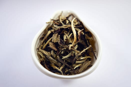 Dry Chinese white tea in a white porcelain bowl close-up