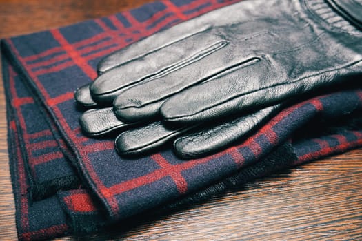 Men's leather gloves and a plaid scarf on a wooden table