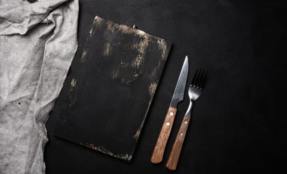 Fork and knife with wooden handle and cutting board on black background