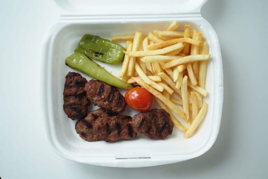 Kabab meat with potato fries in a take away packet on table