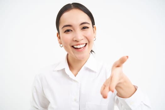 Asian businesswoman extends hand for handshake, team leader introduces herself and smiles friendly, stands confident on white isolated background