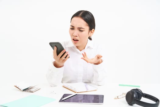 Angry lady boss, businesswoman looks frustrated, talks on mobile phone, has an argument during conversation on cellphone, sits in her office, white background