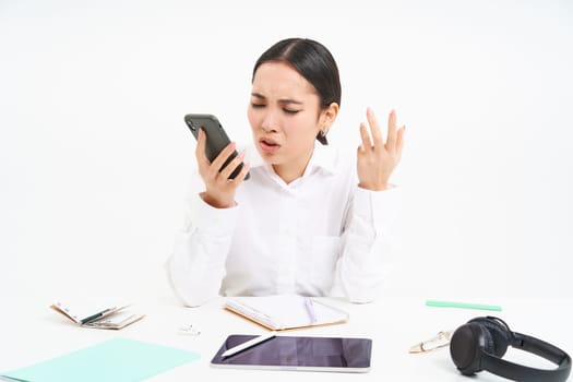 Angry lady boss, businesswoman looks frustrated, talks on mobile phone, has an argument during conversation on cellphone, sits in her office, white background