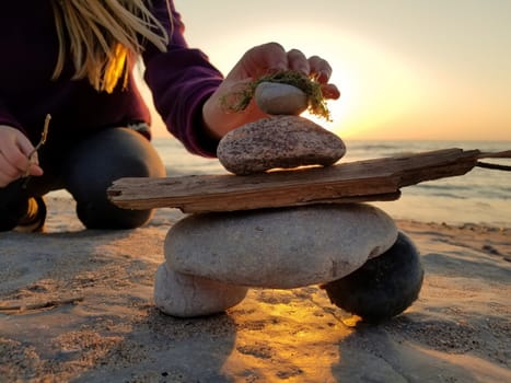 A young girl puts the final rock on an inuksuk inukshuk she's built at the beach at sunset 2