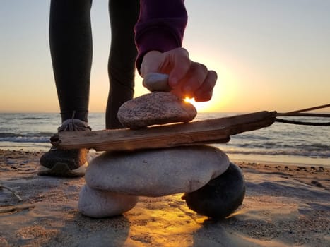 A young girl puts the final rock on an inuksuk inukshuk she's built at the beach at sunset 2