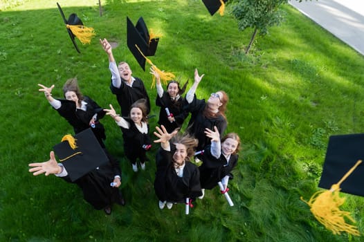 Classmates in graduation gowns throw their caps. View from above.