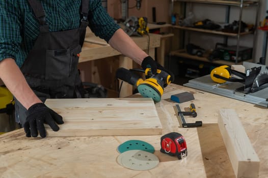 A man using an orbital wood sander in a workshop. Close-up of a carpenter's hands.