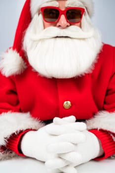 Portrait of santa claus sitting with his arms folded at a white table.