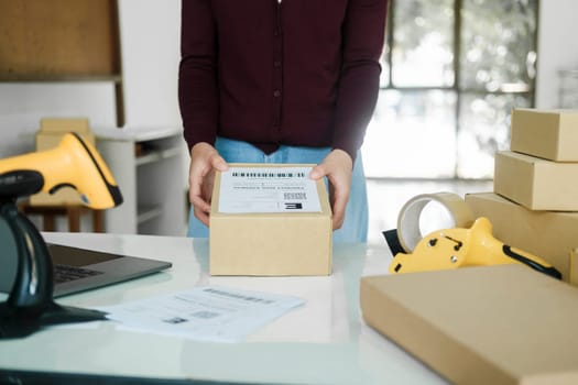 Female online store, business owner putting label tag on parcel.