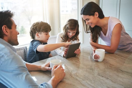 Technology is teaching them to share. a married couple and their young children playing with a tablet together in their kitchen