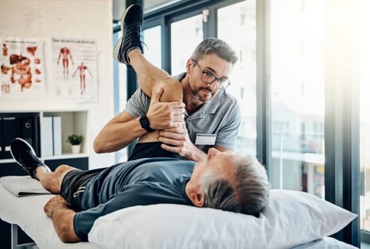 Just one more stretch and were done. a friendly physiotherapist treating his mature patient in a rehabilitation center.