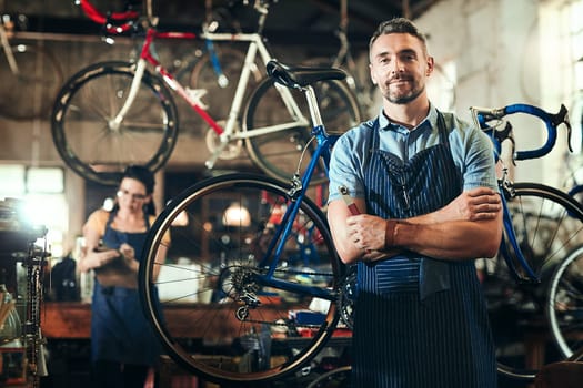 What can I do for you and your bike. Portrait of a mature man working in a bicycle repair shop with his coworker in the background.