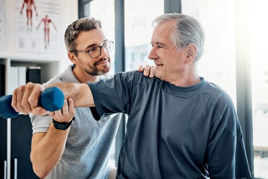 Lets get physical. a friendly physiotherapist helping his mature patient to use dumbbells in a rehabilitation center.
