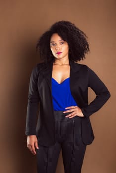Business manager woman dressed in black blazer standing against brown background.