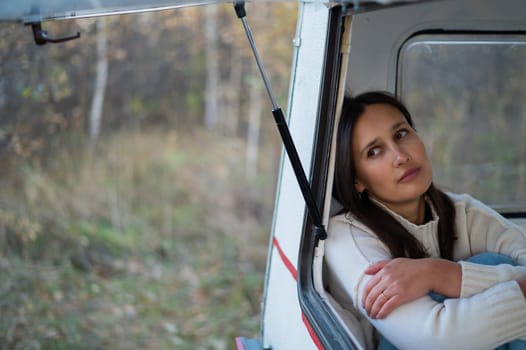 Portrait of a caucasian woman looking out of a trailer window. Travel in a camper in autumn