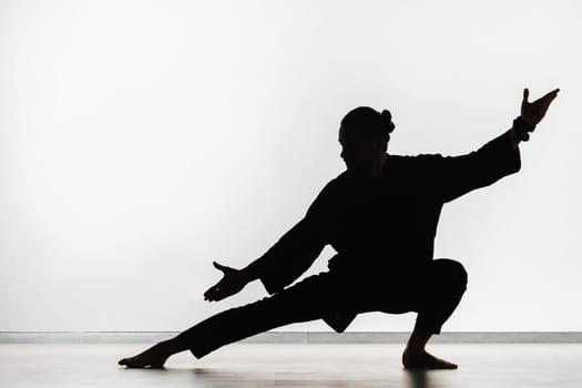 Silhouette of a person practicing qigong energy exercises on a light background