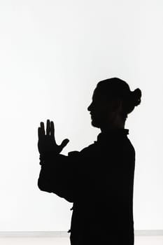 Silhouette of a person practicing qigong energy exercises on a light background