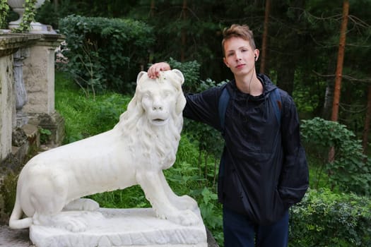A cute boy is standing near a stone statue of a lion.