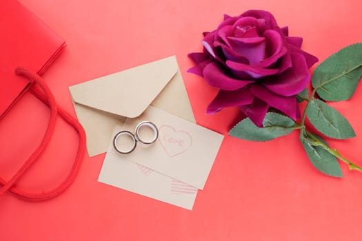 wedding ring and gift box and rose flower on red