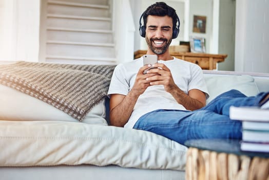 Awesome songs for solo time. a man relaxing on the sofa while using his phone and headphones.