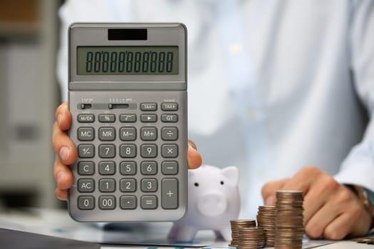 Businesswoman holding calculator on table drains coins and piggy bank