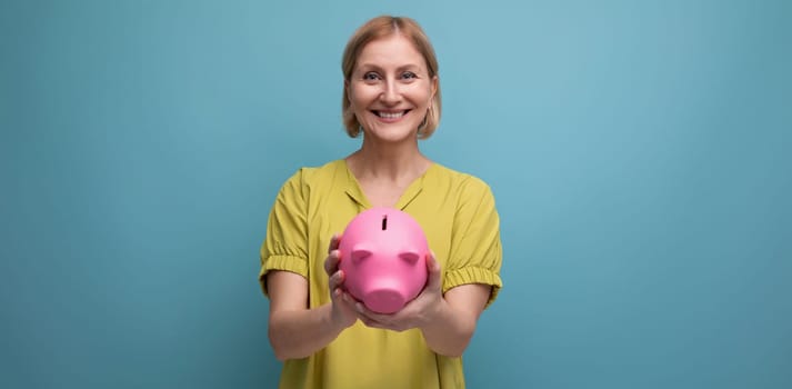 successful blonde mature woman keeps money in a piggy bank and thinks where to invest it