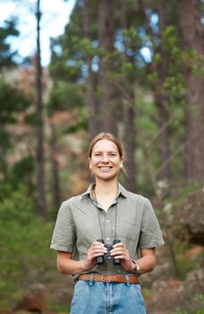Binocular, nature and portrait of happy woman hiking in forest journey, jungle adventure and travel or outdoor explore. Face of a young person birdwatching and trekking in eco friendly, green woods