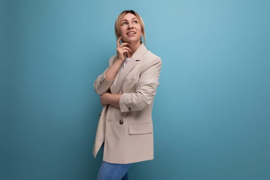 dreamy blonde young adult in beige jacket on studio background with copy space