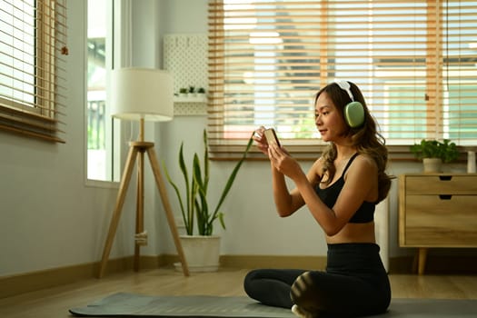 Attractive sportswoman wearing headphone using smart phone on yoga mat. Sport, technology and healthy lifestyle
