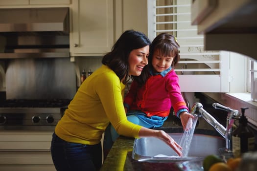 Clean fun starts here. a young mother and her daughter running water in the kitchen sink.