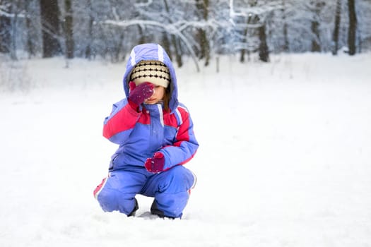 Cute thoughtful sad child in blue jumpsuit in a winter meadow in the forest