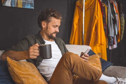 Man taking break at home, enjoying cup of coffee while focused on phone. Concept of spending time at home is emphasized, highlighting the importance of relaxation and leisure in our daily routines.
