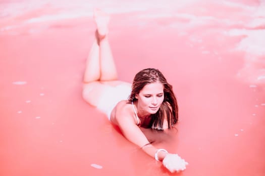 Woman in a pink salt lake. She lies in a white bathing suit. Wanderlust photo for memory