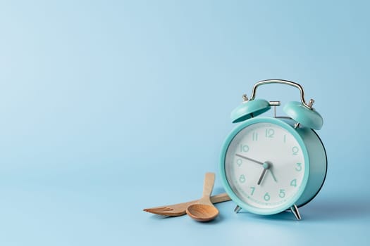 An alarm clock with cutlery set against blue background