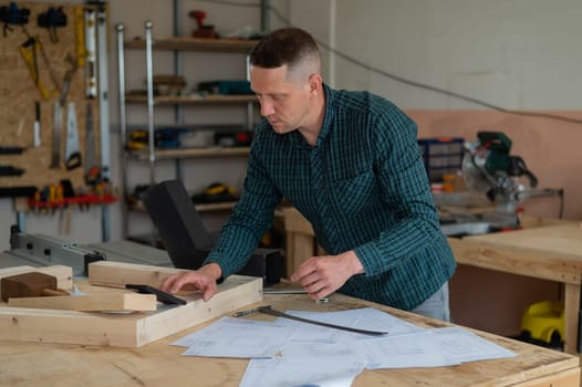 Portrait of a carpenter in a plaid shirt working on a plan in a workshop.