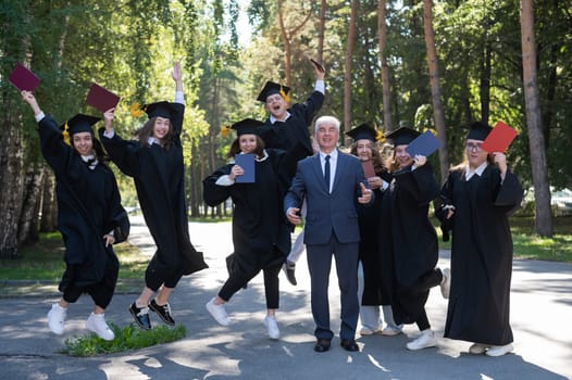 A university professor and seven robed graduates are jumping outdoors.