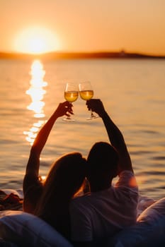 Silhouettes of a happy couple raising glasses on a summer evening near the sea at sunset