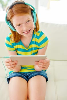 No boredom here. a little girl using a digital tablet with headphones at home.