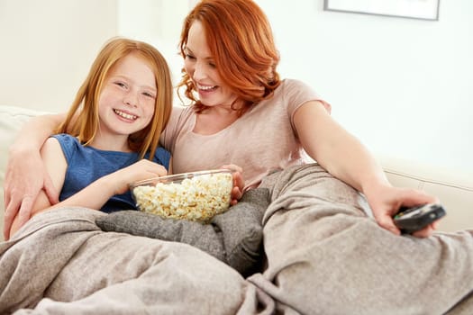 Mommy let me choose the movie tonight. a mature woman and her young daughter watching a movie and eating popcorn on the sofa.