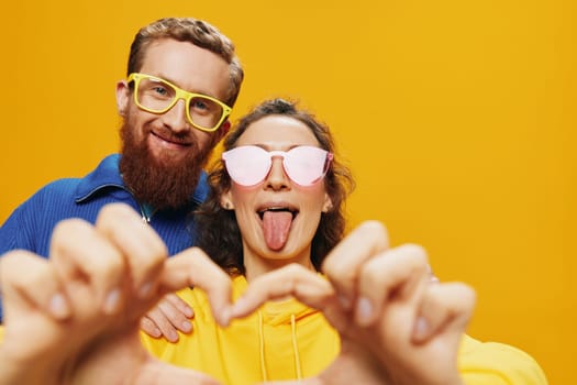 Man and woman couple smiling cheerfully and crooked with glasses, on yellow background, symbols signs and hand gestures, family shoot, newlyweds.