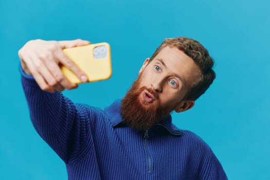 Portrait of a man with a phone in his hands blogger takes selfies, on a blue background. Communicating online social media, lifestyle. High quality photo