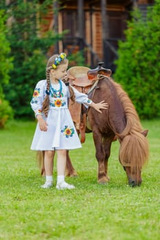 young girl in Ukrainian national dress strokes a pony