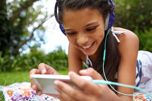 Entertainment for everywhere. a young girl listening to music on her cellphone in the outdoors.