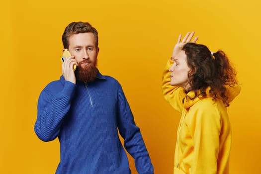Man and woman couple with phone in hand call talking on the phone, on a yellow background, symbols signs and hand gestures, family quarrel jealousy and scandal.